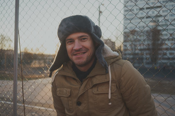 Happy handsome young man in cap with earflaps. The young man in the fur hat. a young guy standing...