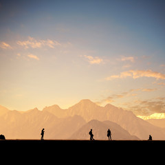 Fototapeta na wymiar Silhouetted people over mountains and sunset sky