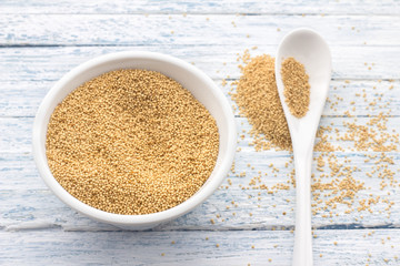 Raw amaranth seeds in a ceramic bowl on a light blue background, top view, selective focus