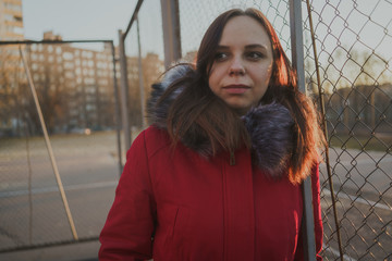 Happy beautiful young girl in a red jacket posing outside on a cloudy day. emotional portrait of a student. street style