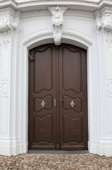 Eingangsportal mit braunen Flügeltüren und Verzierungen im Mauerwerk