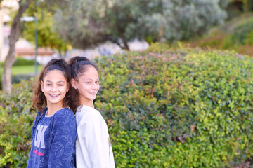 Lifestyle people concept: two pretty young school sisters teenage girls.Two young happy hipster girl friends with ponytail standing together and having fun. Over green nature background.