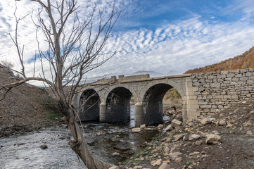 Old bridge in ruins that is generally flooded by the waters of the reservoir of Riaño in Leon, Spain. In the background you see the mountains between the morning mists. There is a tree near the bridge