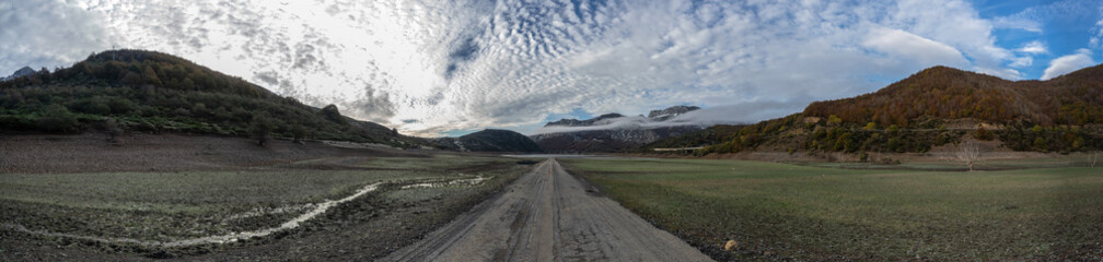 Panoramic photo of a valley with a old ruined road that is generally flooded by the waters of the reservoir of Riaño in Leon, Spain. In the background you see the mountains between the morning mists.  - obrazy, fototapety, plakaty