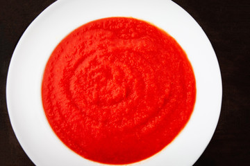 Tomato soup in a white plate on dark background, Macro