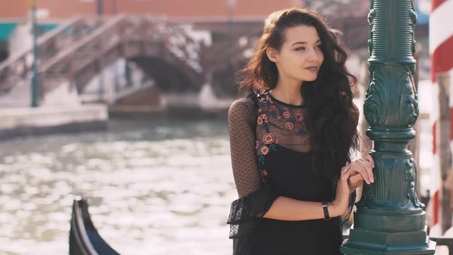Seductive romantic woman standing on the pier against beautiful view on venetian chanal with boats and gondolas in Venice, Italy. Slow motion 4k footage. Gorgeous mixed race Asian Caucasian female in