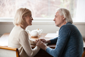 Loving senior couple have romantic moment looking in eyes, sensual aged husband and wife holding hands giving support and care, elder man and woman caress, comforting each other. Relationships goal