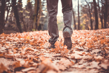 Feet shoes walking on fall leaves outdoor with autumn season nature (color toned image)