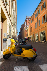 Fototapeta na wymiar Yellow old fashioned scooter on street in Rimini with many-coloured houses, ancient city center. Vacation in beautiful Italy, Europe.