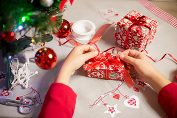 Hands of young woman wrapping some presents / gifts to beautiful stylish christmas paper with a red...