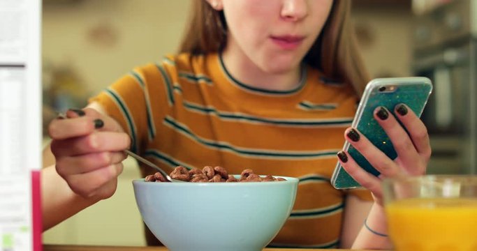 Teenage Girl Eating Unhealthy Bowl Of Sugary Breakfast Cereal Texting On Mobile Phone