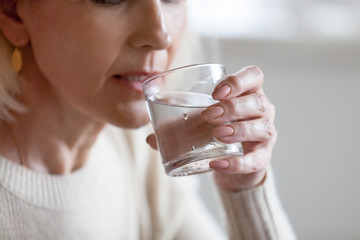 Aged woman holding glass feeling thirsty or dehydrated, senior female drinking fresh pure aqua...
