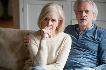 Emotional senior husband and wife watch sad movie relaxing on cozy sofa at home, sensitive aged...