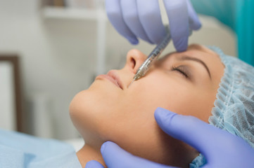lateral view of lips augmentation procedure on a young woman done by a cosmetologist doctor with...