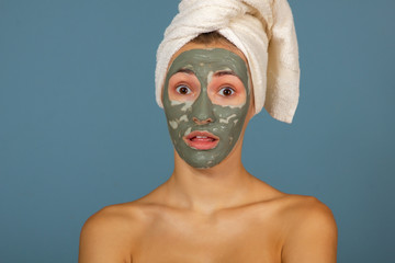 Beautiful cheerful teen girl applying facial clay mask. Beauty treatments, isolated on blue background.
