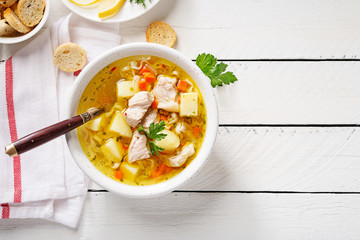 Chicken soup with noodles and vegetables in white bowl on white  wooden background