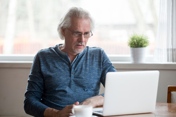 Confused senior male use laptop looking at screen shocked by received message or letter, stunned...