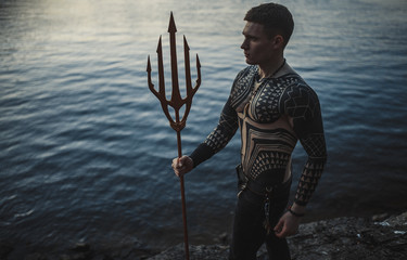 A young man with a trident against the background of water. - obrazy, fototapety, plakaty