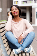 Fototapeta premium smiling young black woman sitting outside and talking with mobile phone