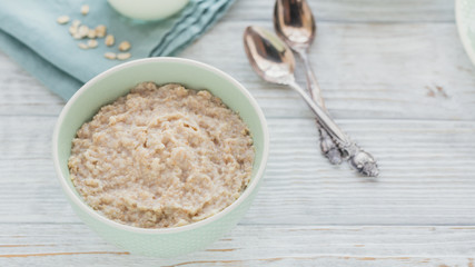 Oatmeal porridge bowl on the white wooden background.