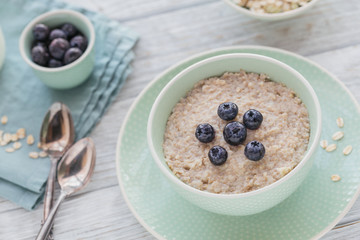 Oatmeal porridge bowl on the white wooden background.