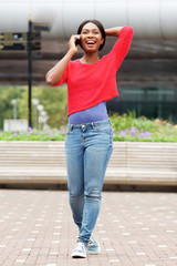 Obraz premium Full length carefree young black woman walking with cellphone in the city