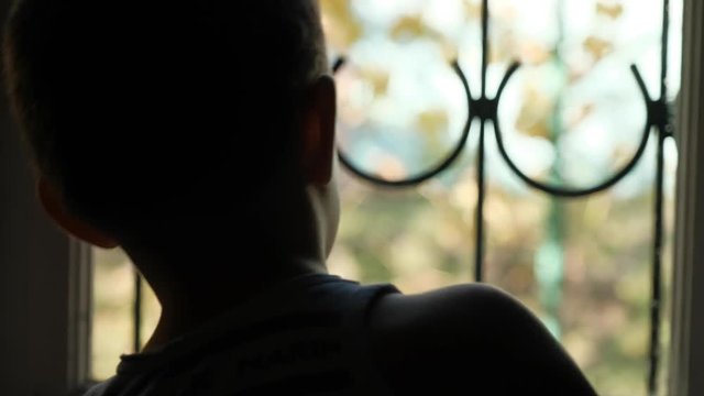 The boy is 3-5 years old outside the window with a lattice