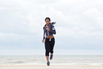 Full body sporty african american woman running by the beach