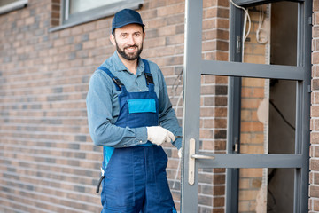Builder in uniform installing a door lock into the entrance door of a new house outdoors