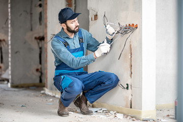 Electrician mounting wiring for electric sockets on the construction site of a new building indoors