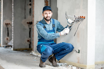 Portrait of an electrician mounting wiring for electric sockets on the construction site of a new building indoors