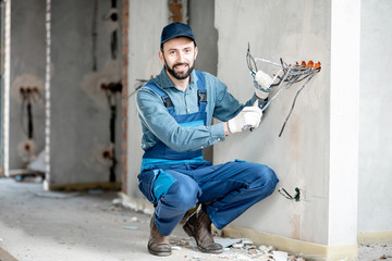 Portrait of an electrician mounting wiring for electric sockets on the construction site of a new...