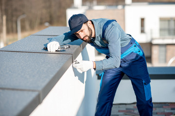 Builder in uniform mounting metal cover on the parapet of a new building - obrazy, fototapety, plakaty
