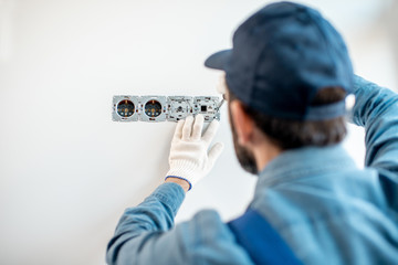 Electrician in uniform mounting electric sockets on the white wall indoors