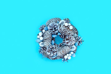 Winter and Christmas wreath with snow covered spruce pine fir, mistletoe, pine cones, cedar isolated on blue background. Top view