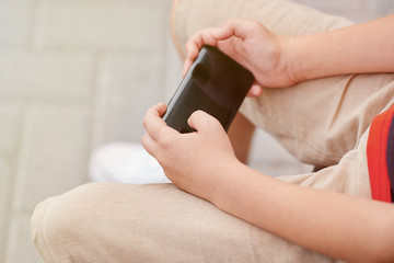Child sitting outside school and playing games on his cell phone
