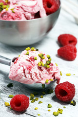 Raspberry ice cream scoop with chopped nuts and white chocolate on a rustic background