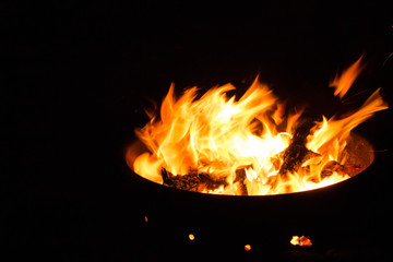 Beautiful flame with sparks in bonfire in the night. Heat and danger energy concept. Fire in darkness. Inferno and element concept. Campfire with bright flame. Fire in motion on black background.  