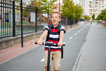 School boy in riding with his electric scooter in the city with backpack on sunny day. Child in colorful clothes biking on way to school