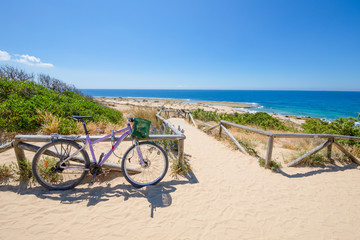 purple bicycle parked next to beach access in sand walkway down to the ocean coast in Cape...