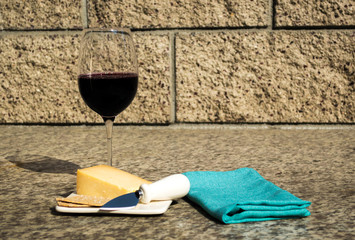 red wine, cheddar cheese, crackers and knife on a small plate next to a green linen napkin on an outdoor marble counter with copy space