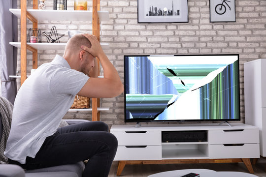 Frustrated Man Looking At Broken TV