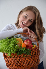 Young smiling woman with a grocery shopping basket isolated on white background. Girl with basket of vegetables and fruits on a white background.