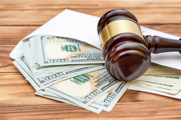 Dollar bills in white envelope and judge's gavel on wooden background.