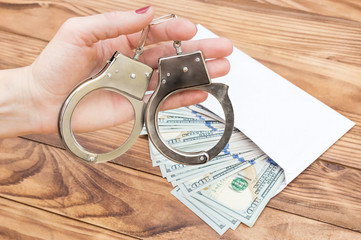 Woman's hand holding handcuffs over table with money in envelope.