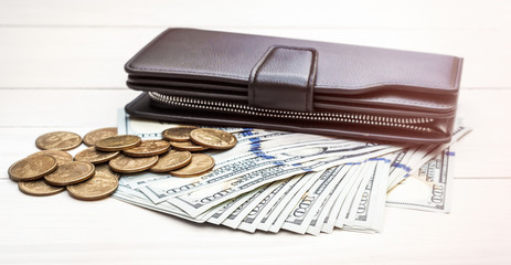 Black purse with dollar bills and coins on wooden table. Toned image.