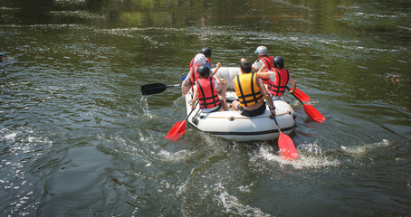 Group of men and women, enjoy water rafting activity at river. Rafting family on holidays