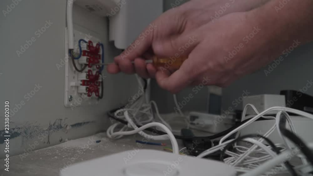 Poster electrician hands using a screwdriver to secure wires to the wall socket.