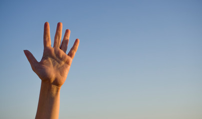 Woman's hand isolated on blue background in summer sky nature. Stop, help, fifth concept with hand up. Gesture symbol number five in sign language. Say hello / hi or goodbye concept with copy space.