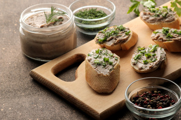 Fresh homemade chicken liver pate with greens on bread on a dark background. A sandwich.